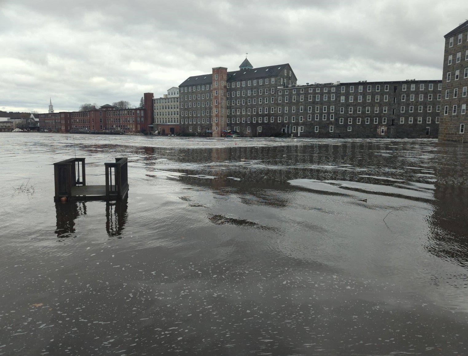 A river over tops is banks and flows by an old mill building.