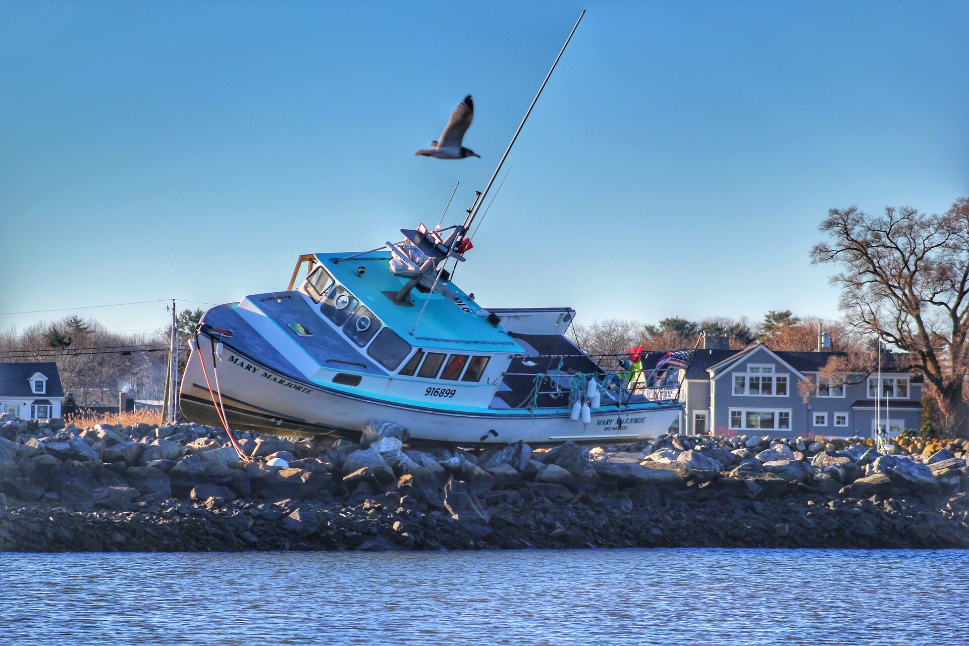 A lobster boat rests on its side up out of the water on a rocky shoreline.